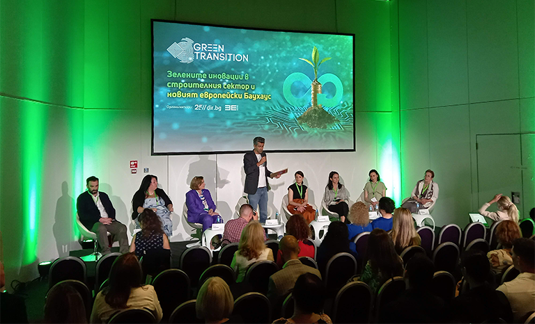 от далечен кадър на участник в събитието GREEN WEEK 2023, говорещ по темата "Зелените иновации в строителния сектор и новият Европейски БАУХАУС". Около него седят и слушат други участници в събитието.